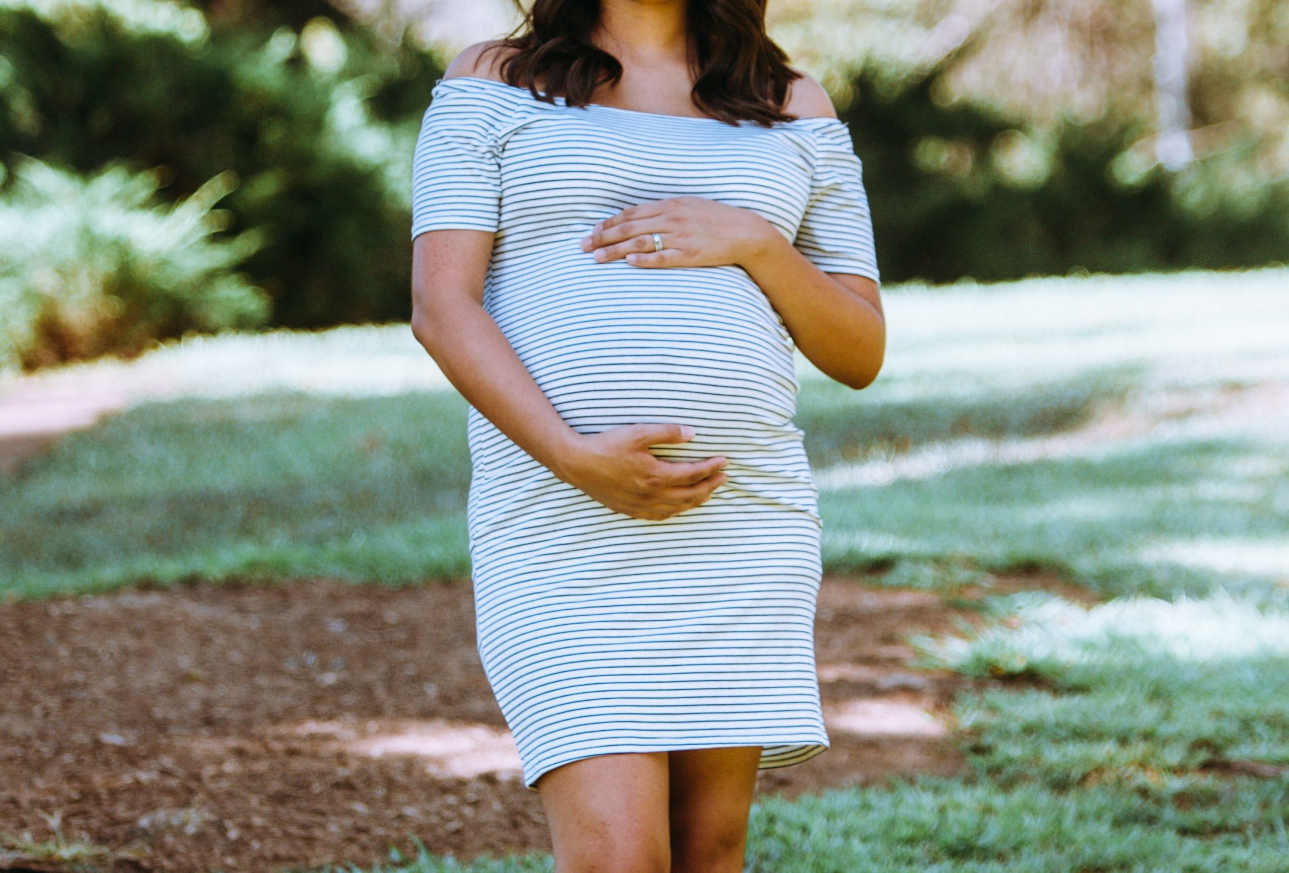 Surrogate mother in a striped dress standing in a park.