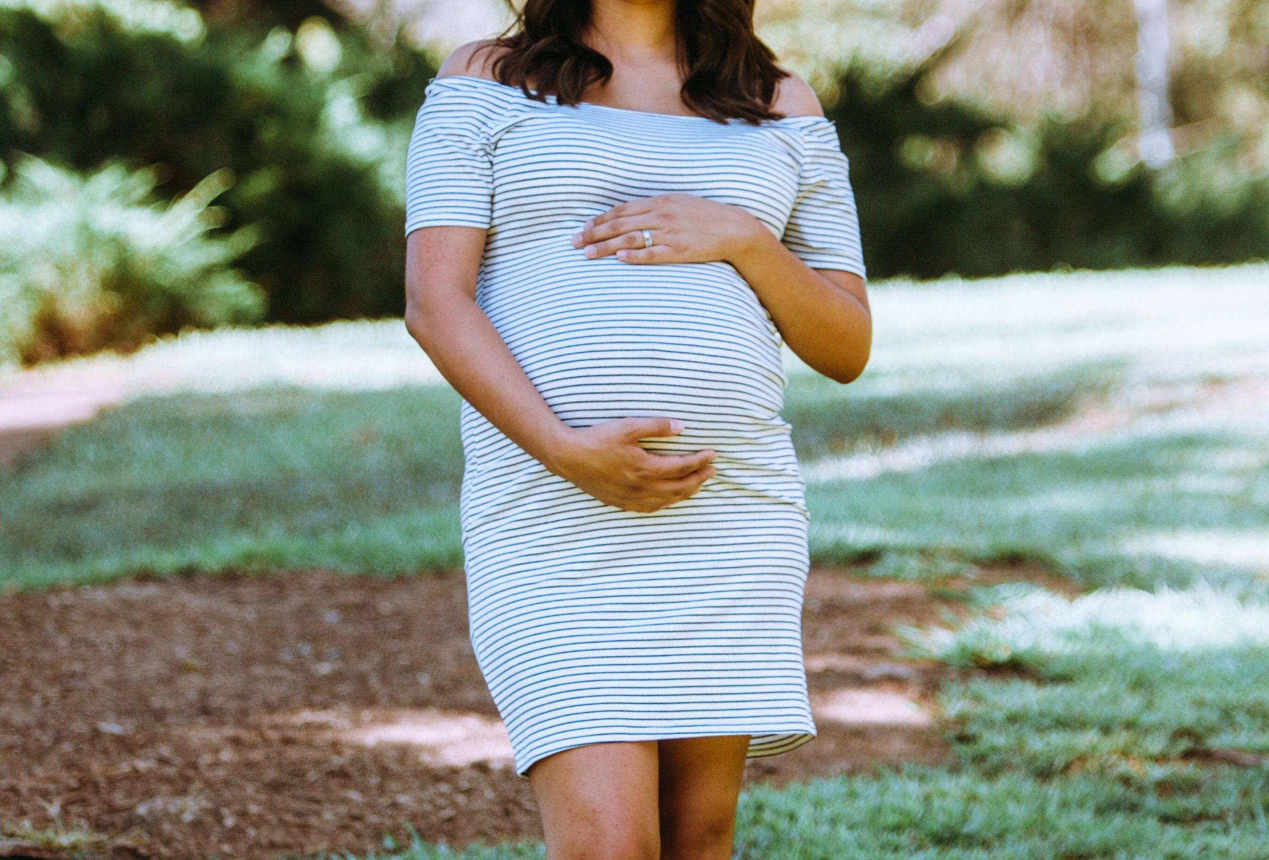 Mãe substituta em um vestido listrado em pé em um parque.