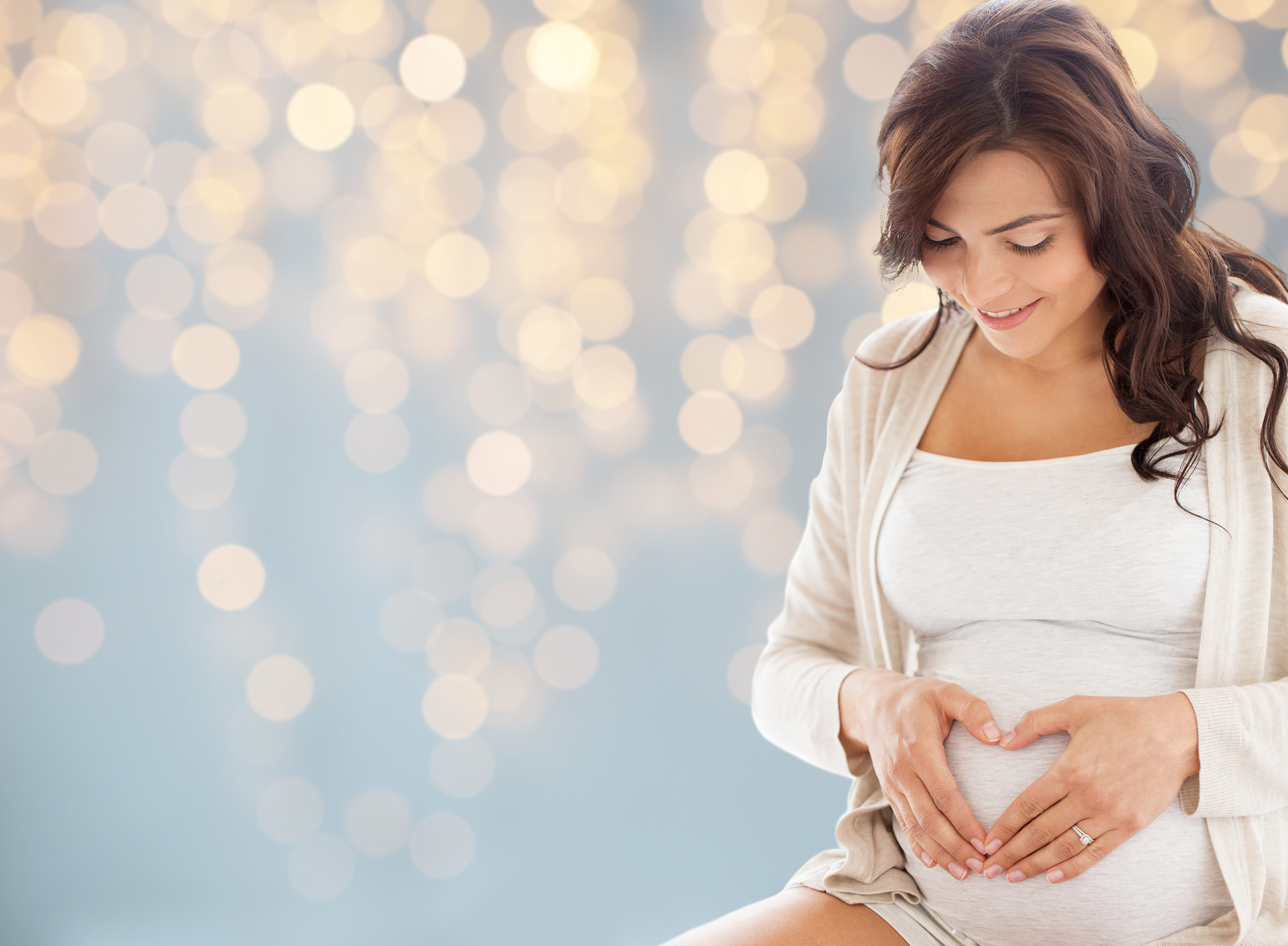 happy pregnant woman making heart gesture in bed