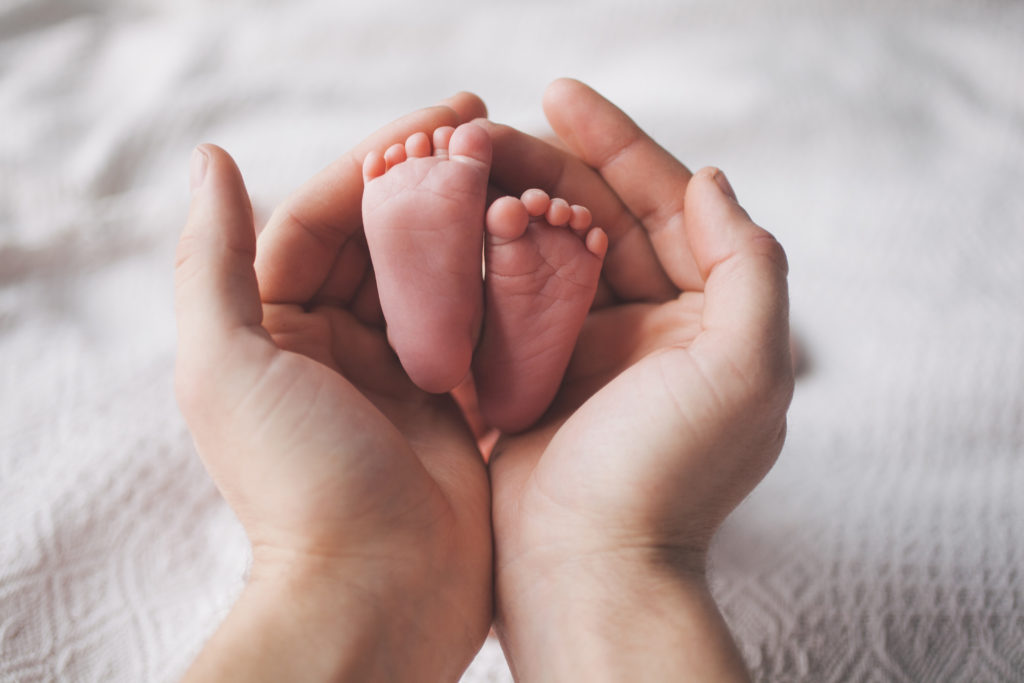 Pai segurando nas mãos os pés do bebê recém-nascido.