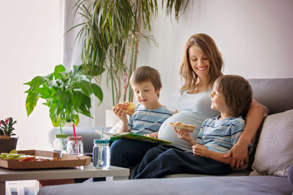 Família jovem feliz, mãe grávida e dois meninos, comendo p saboroso