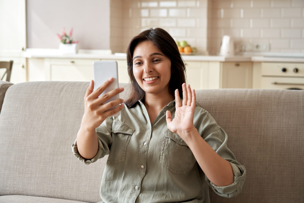 Femme en chemise verte appelant par vidéo et saluant l'appareil photo de son smartphone.