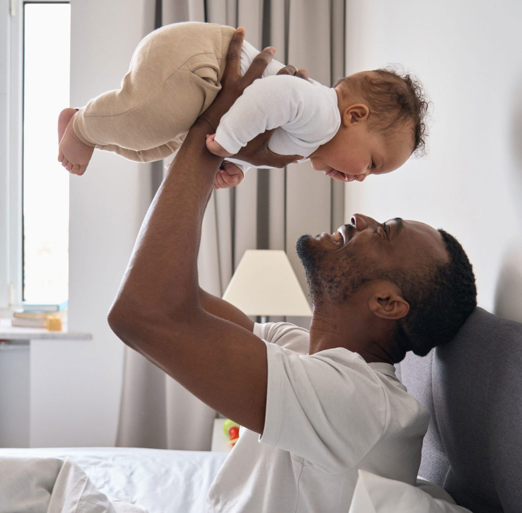 Man lifting a happy baby in the air at home.