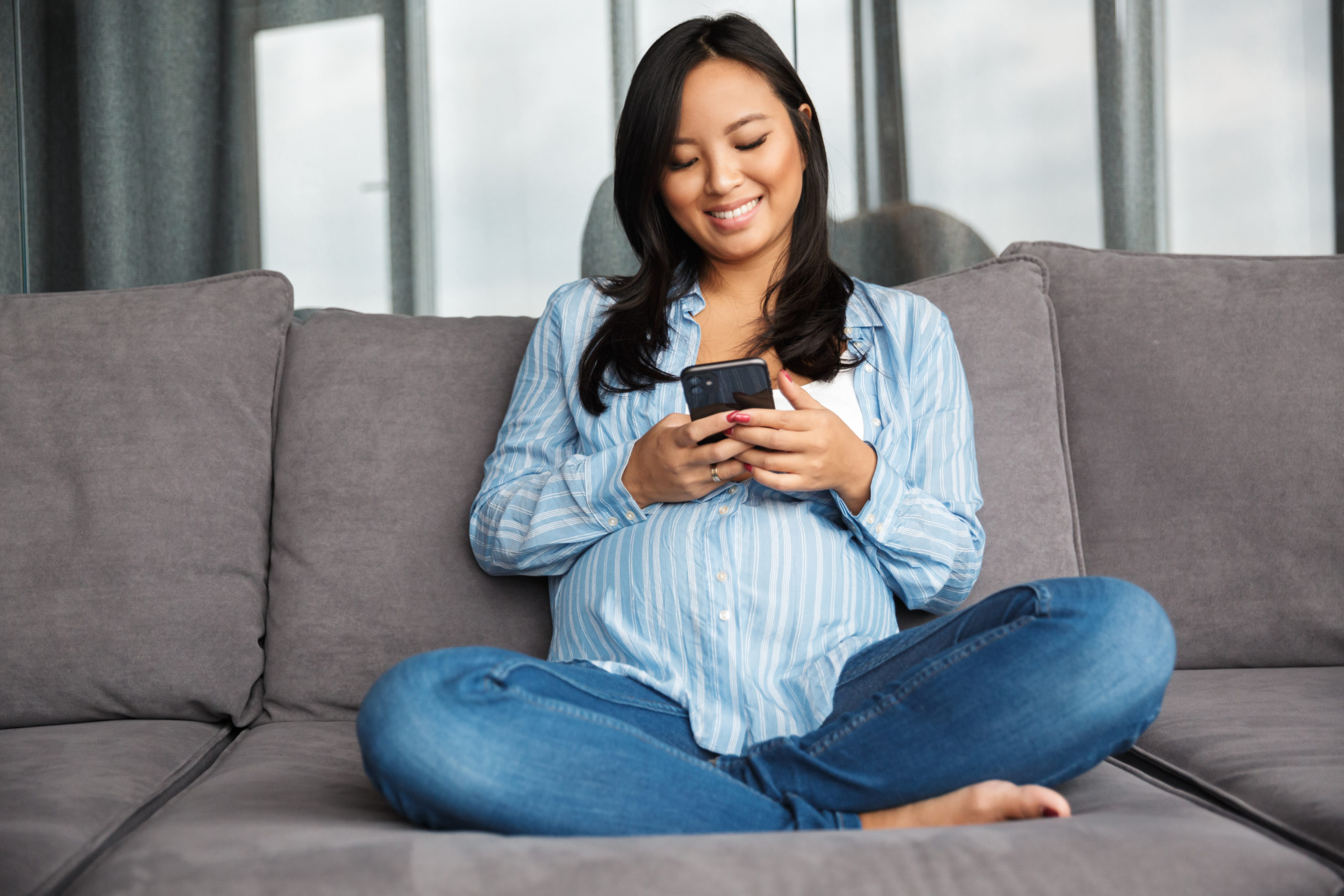 صورة لامرأة حامل مرحة تبتسم وتستعمل الهاتف المحمول