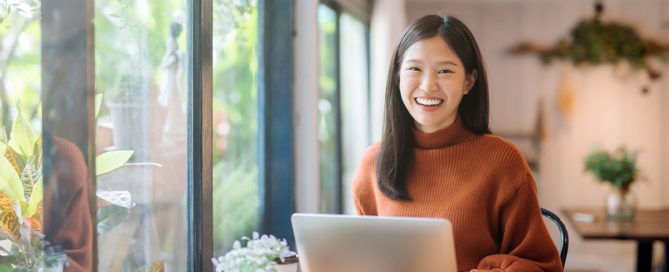 gelukkige jonge aziatische vrouw die haar laptop met behulp van