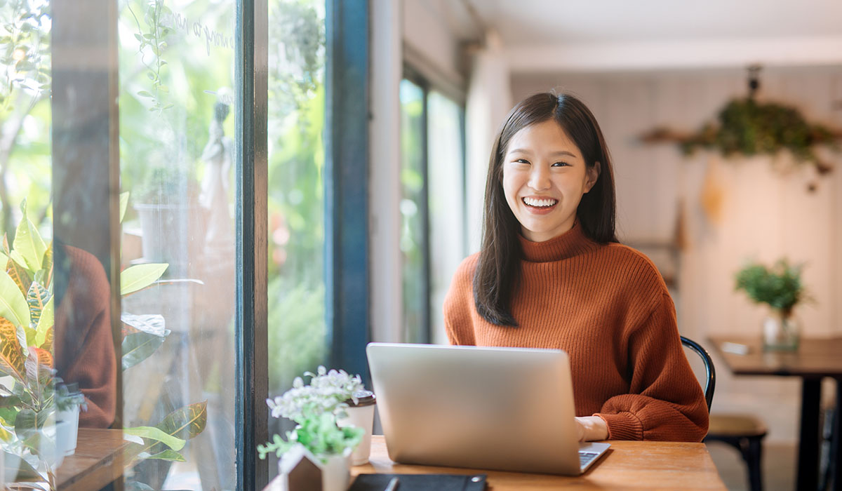 gelukkige jonge aziatische vrouw die haar laptop met behulp van