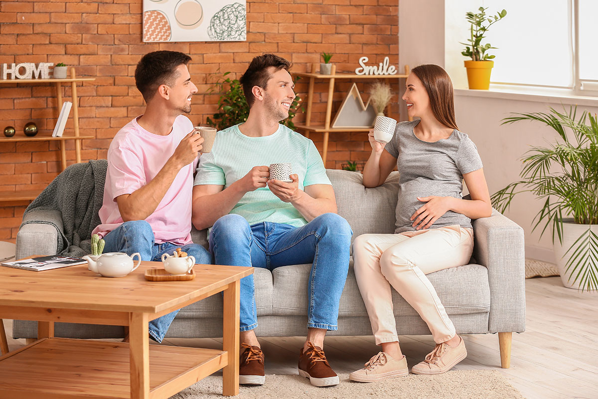 Werdende LGBTQIA+-Eltern unterhalten sich bei einem Kaffee zu Hause freundschaftlich mit einer schwangeren Leihmutter.
