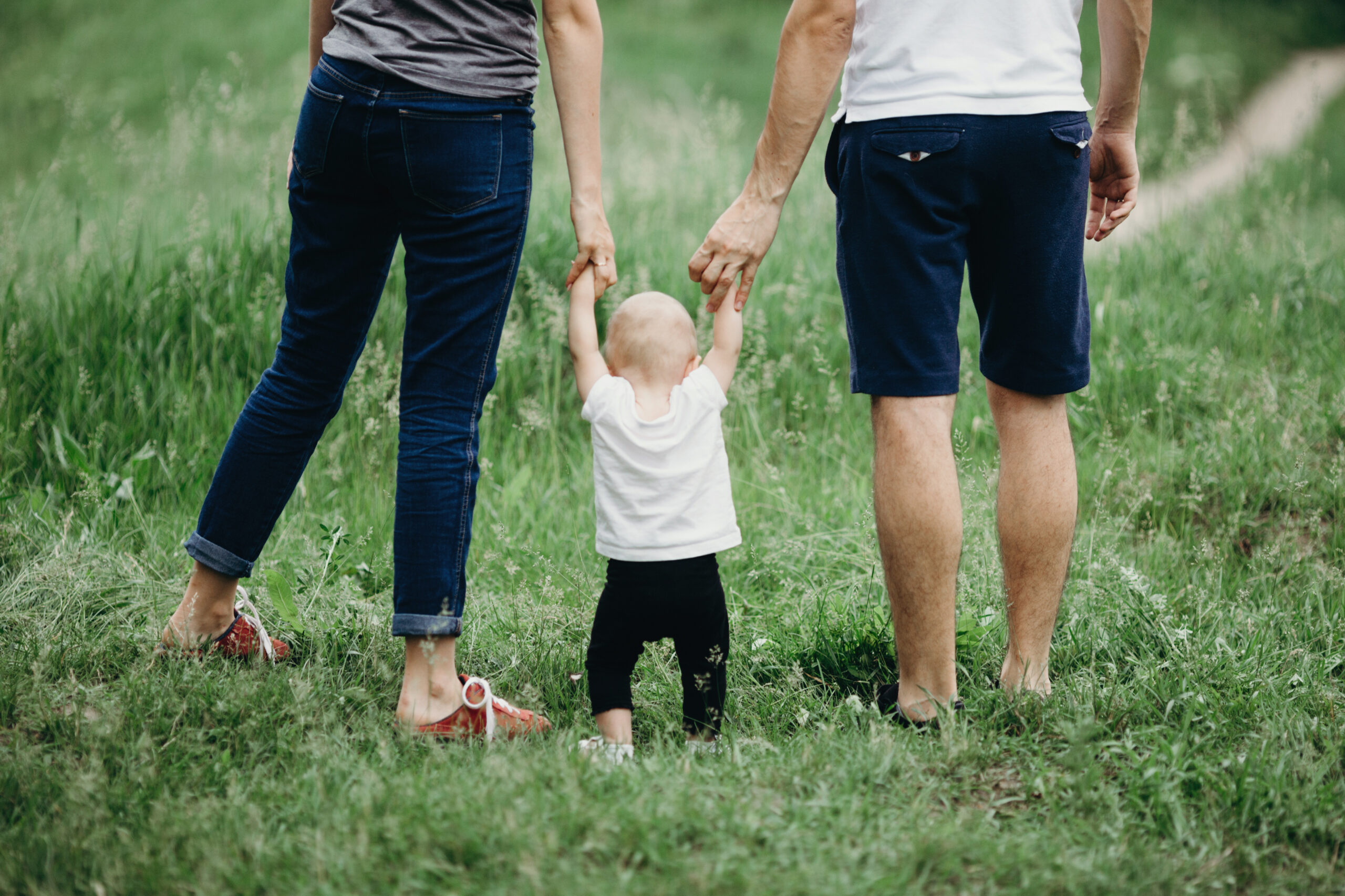 Niño caminando tomados de la mano con sus padres al aire libre sobre el césped.