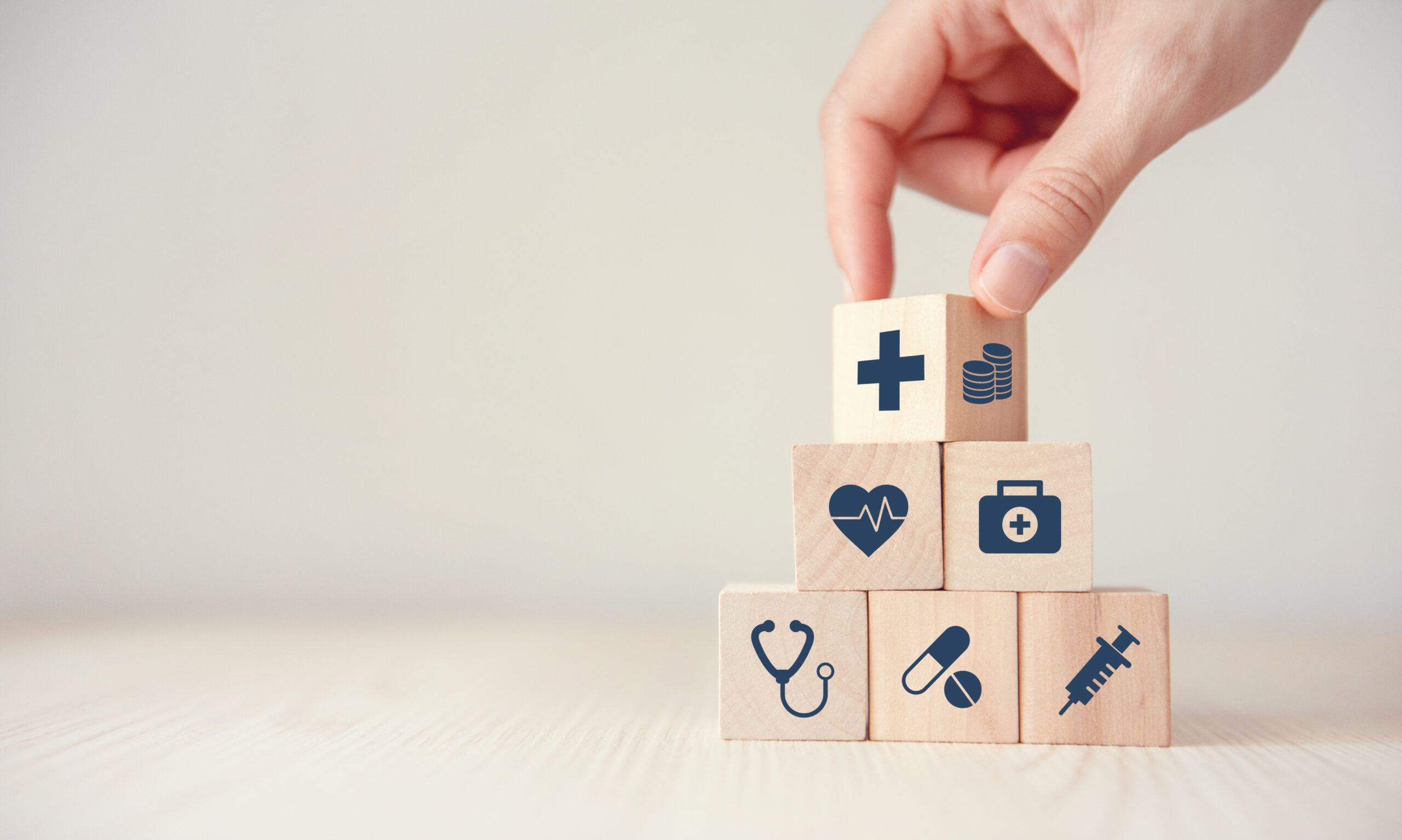 Hand stacking wooden blocks with health and medical icons.