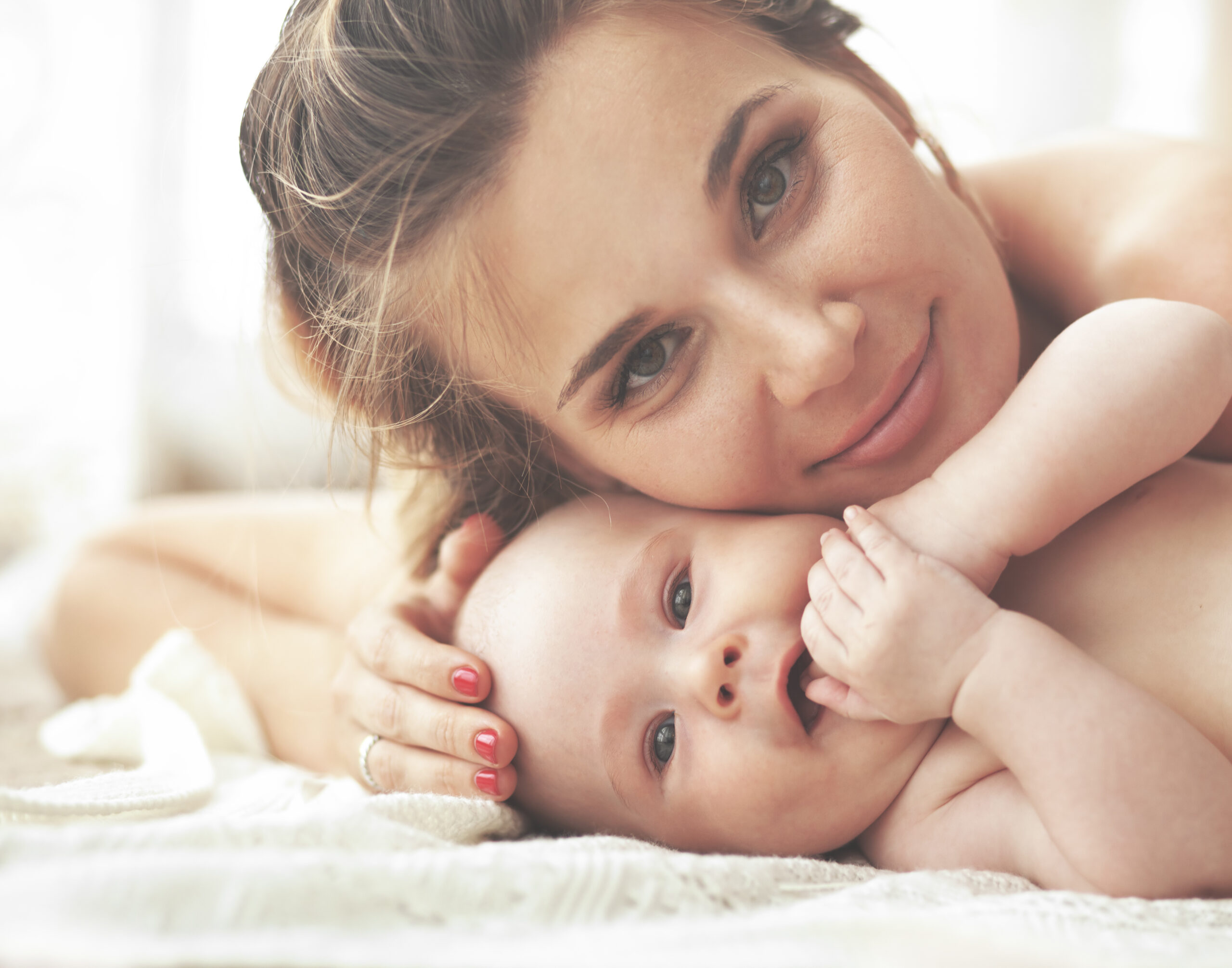 Mãe e bebê deitados de frente para a câmera em contato próximo e afetuoso.